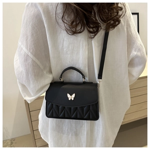 Detail of black crossbody bag with white butterfly clasp and V-shape quilting texture