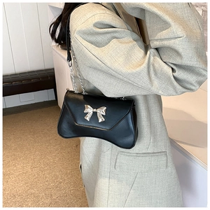 Close-up of black crossbody bag with metallic bow clasp and leather chain strap