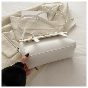 Detail of white leather crossbody bag featuring gold bow hardware and top handle