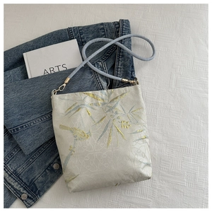 Close-up of golden bamboo and bird embroidery on white silk fabric of a handbag