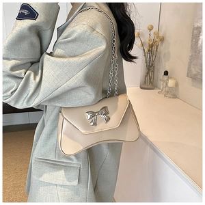 Detail view of beige leather shoulder bag featuring a silver metal bow buckle accent