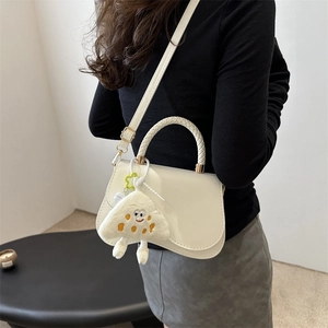White leather shoulder bag with woven handle and cute cartoon charm shown on model