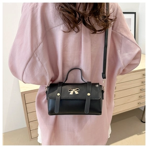 Detail of a black leather handbag with a gold bow buckle and studded strap accents