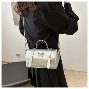 Detail of silver crossbody bag with golden bow clasp and metallic mirror finish on model