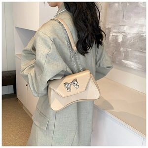 Detail of beige crossbody bag with silver bow ornament and leather chain strap