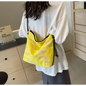 Détail d'un cabas jaune vif avec motifs ondulés gaufrés et bandoulière noire sur modèle
