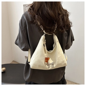Dettaglio di una borsa hobo in velluto crema con ciondolo a fiocco argento e perla ambra