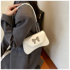 Detailed view of white shoulder bag featuring a silver metal bow buckle and chain strap