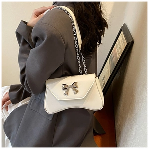 Side view of white leather crossbody bag with silver bow accent on a fashion model