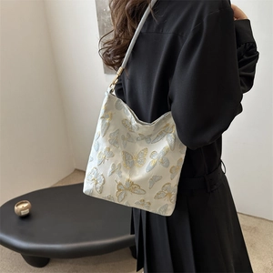 Elegant white shoulder bag with gold butterfly embroidery shown on a model's shoulder