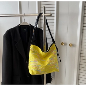 Détail du sac cabas en jacquard gaufré jaune avec broderie ondulée sur un cintre