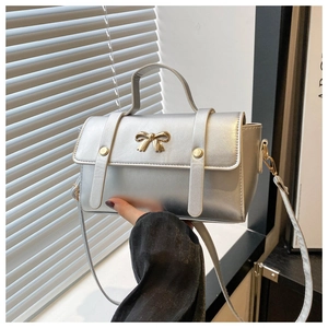 Close-up of metallic silver crossbody bag with golden bow hardware and rivet detail