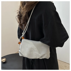 Détail du sac plissé gris avec perles d'ambre sur la fine bandoulière réglable