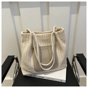 Detail of woven straw tote bag with brown leather patch and rope handles on book
