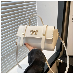 Detailed view of white leather crossbody bag with golden bow hardware and hand handle