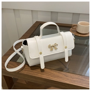 Detail of white crossbody bag with golden bow hardware on an elegant wooden table