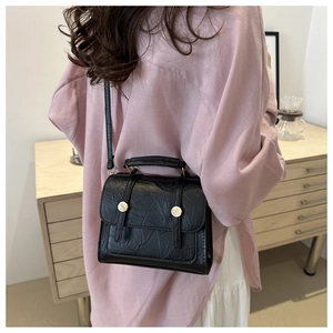 Detailed view of black textured faux leather crossbody bag with golden metal buckles