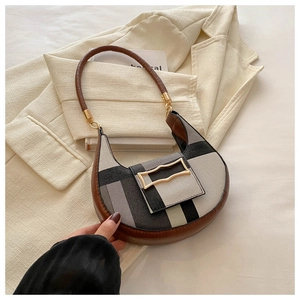 Detail of color-block striped fabric and brown leather handle on a crescent handbag