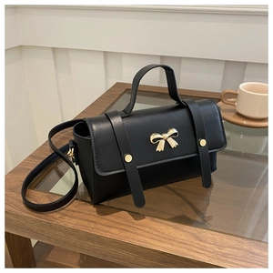 Close-up of black PU leather handbag featuring golden bow hardware and stud details