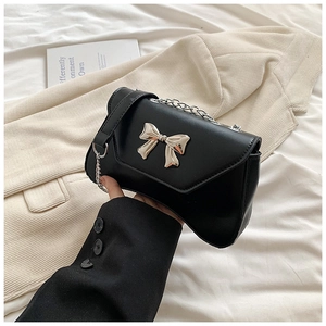 Detail of a black leather shoulder bag featuring a silver metal bow buckle and chain strap