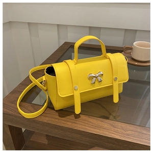 Close-up of bright yellow crossbody bag with silver bow detail on a stylish wooden table
