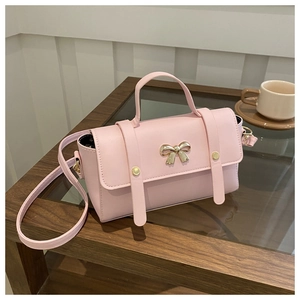 Pink faux leather crossbody bag with golden bow hardware detail on a cafe table