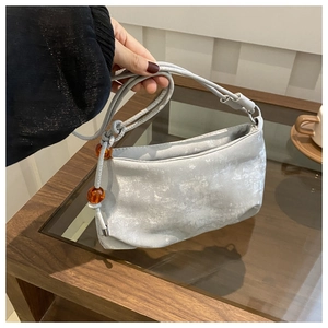 Détail d'un sac à bandoulière argenté texturé avec perles oranges sur fond de table