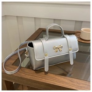 Close-up of a silver metallic crossbody bag with golden bow decoration on a coffee table