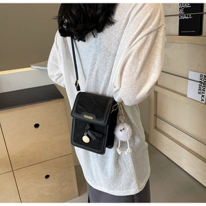 Close-up of black textured mobile phone crossbody bag with plush charm on a female model