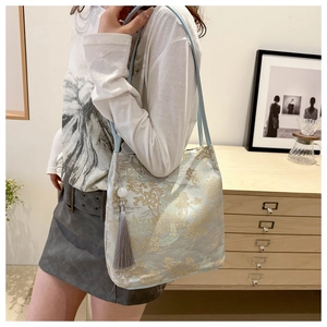 Dettaglio della borsa tote in broccato celeste con ricami paesaggistici e nappa grigia
