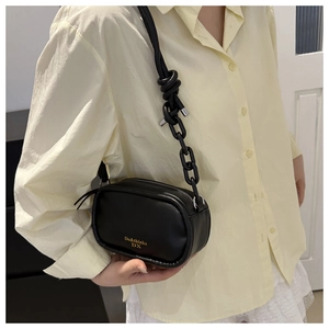 Detail view of black oval crossbody bag featuring unique knot rope and chain strap
