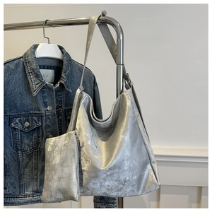 Detail of silver metallic hobo bag and small pouch set against blue denim jacket