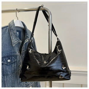 Close-up of black patent leather hobo bag with embossed texture and metal butterfly accents
