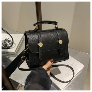 Detail of black textured crossbody bag with gold hardware and top handle design