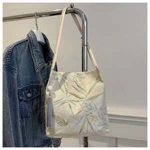 Dettaglio ricamo foglie di bambù su borsa tote in tela color crema con nappa