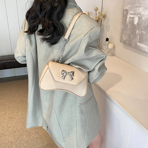 Elegant beige crossbody bag with silver bow accent and chain strap shown on model