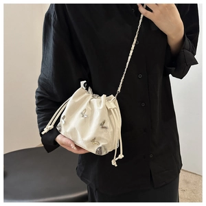 Detail of a creamy white drawstring bucket bag with silver butterfly charms and chain strap