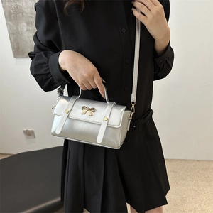 Silver square crossbody bag with gold bow clasp shown on a model for a stylish look