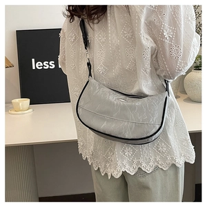 Silver wrinkled moon bag with wide black strap worn over a white embroidered top