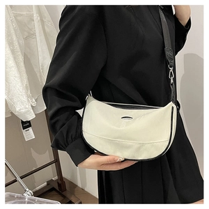 Detail of a cream-colored crescent bag with black piping and stylish wide shoulder strap