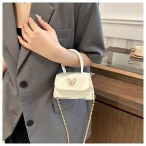 Detail of cream mini crossbody bag featuring a golden bow buckle and elegant chain strap