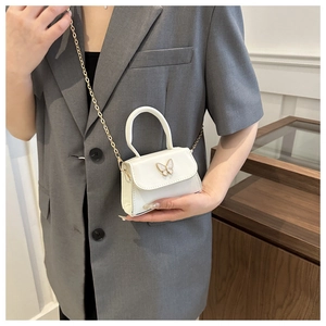 Close-up of a white mini flap bag featuring a metal bow buckle and a gold chain strap