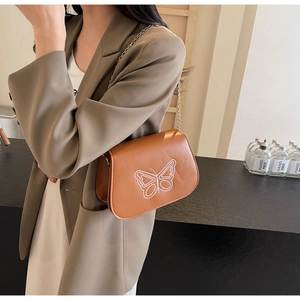 Détail de broderie papillon blanc sur un sac à bandoulière marron avec chaîne dorée
