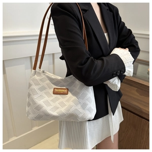 Detail of white textured fabric shoulder bag with brown leather straps and gold lettering