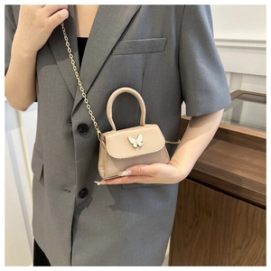 Detail view of a beige mini crossbody bag with metal bow accent and gold chain strap