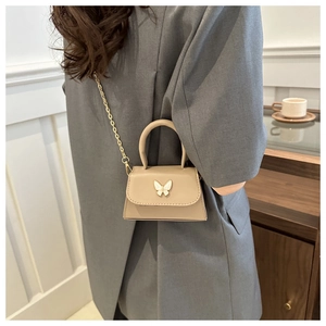 Detail of beige crossbody bag with gold chain and butterfly clasp on grey blazer