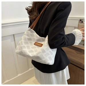 Detail of white woven tote bag with brown leather strap and logo tag for office style
