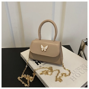 Detail of a beige PU leather crossbody bag with white bow hardware and gold chain strap