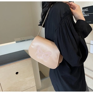 Détail du sac bandoulière beige avec broderie papillon rose et chaîne métallique élégante