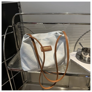 Detail of white textured fabric shoulder bag with brown leather strap on industrial shelf